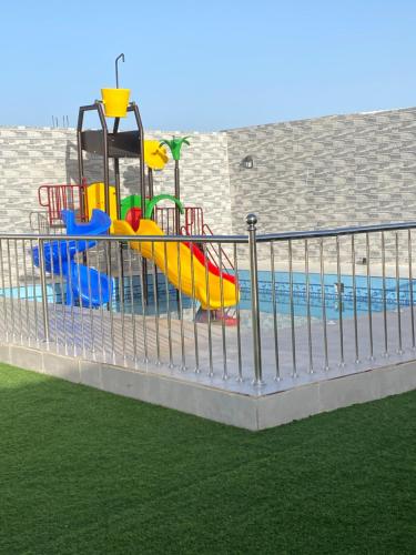 un parque infantil con tobogán junto a una piscina en استراحة الشروق en Al ‘Uqūl