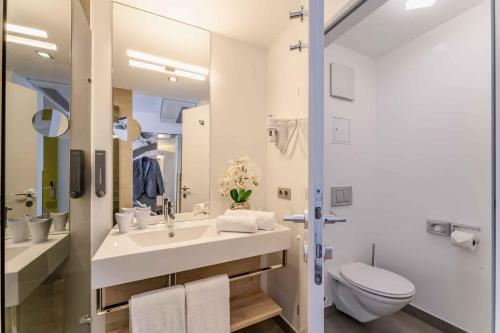a white bathroom with a sink and a toilet at PLAZA INN Wien Gasometer in Vienna