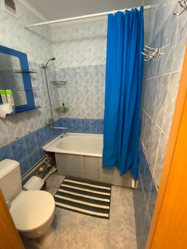 baño con bañera, aseo y cortina de ducha azul en Квартира на Сейфуллина, en Baljash