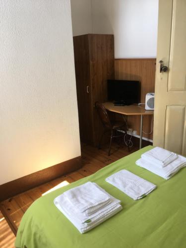 a room with a bed with green sheets and a desk at Alojamento Local Duarte's in Coimbra