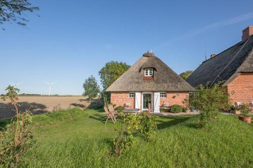 ein altes Haus mit einem Strohdach auf einem Feld in der Unterkunft Idyllische kleine Reetdachkate mit Blick über die Felder - Kamin, Terrasse & Privatparkplatz in Simonsberg