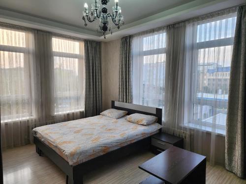 a bedroom with a bed and a chandelier and windows at Apartment KG in Bishkek