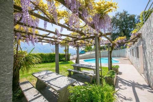 einem Picknicktisch und einer Bank unter einer Pergola mit lila Blumen in der Unterkunft Casa Monti Belvedere in Locarno