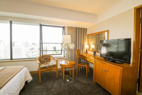 um quarto de hotel com uma secretária, uma televisão e uma cama em Hotel Miramar em Lima