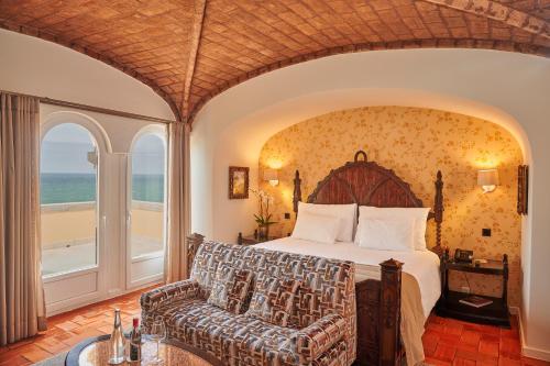 a bedroom with a bed and a couch and a window at Hotel Fortaleza do Guincho Relais & Châteaux in Cascais