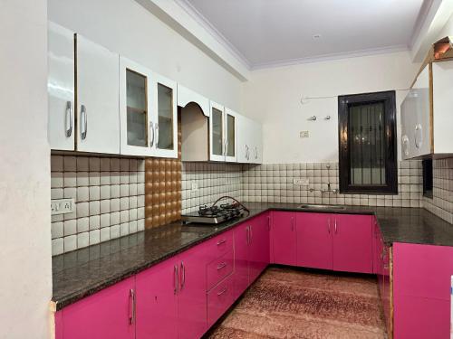 a kitchen with pink cabinets and tile walls at Entire flr 2BHK+terrace near Medanta hospital ggn in Gurgaon