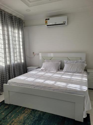 een witte slaapkamer met een groot bed met witte lakens en kussens bij Samnica Guest House in Accra