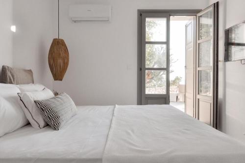 a white bedroom with a large bed and an open door at Cliff Villa in Sarakíniko