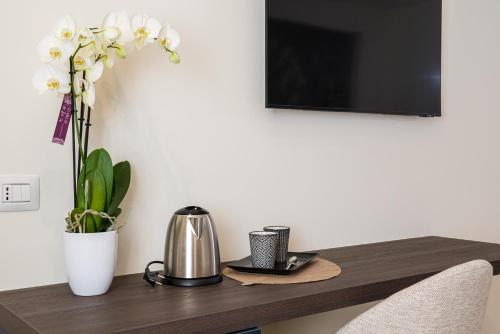 a table with a tv on a wall with a coffee pot and flowers at I Due Mori - Luxury Rooms in Giardini Naxos