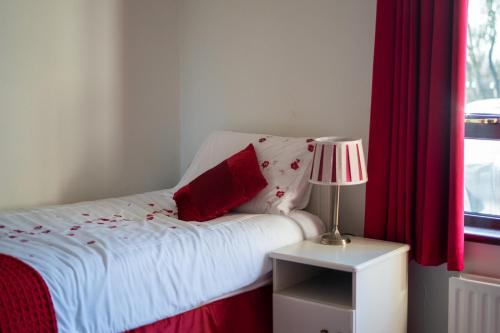 a bedroom with a bed with red curtains and a lamp at Glen Lodge in Ballymoney