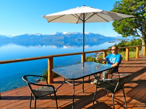 a man sitting on a deck with a table and an umbrella at Terra Luna Lodge in Puerto Guadal