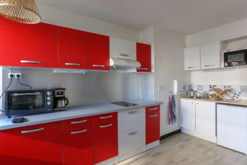 - une cuisine rouge avec des placards blancs et un four micro-ondes dans l'établissement 32 m love nest studio with balcony, à Paris