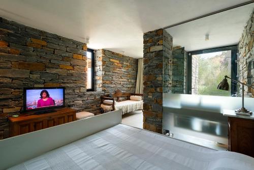 a bedroom with a tv and a stone wall at House garden in Ioulis