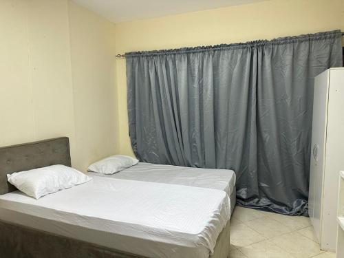 een slaapkamer met 2 bedden en een grijs gordijn bij MIRA ALMAJAZ in Sharjah
