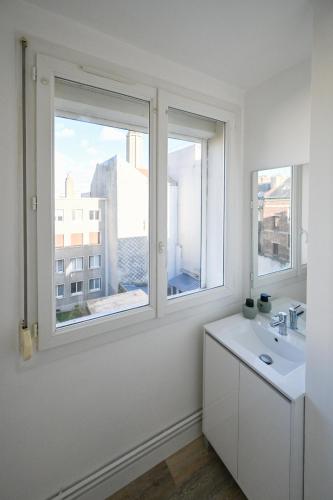 une salle de bain blanche avec un lavabo et deux fenêtres dans l'établissement L'Escale Bleue - Balcon privé - Vue mer, au Havre
