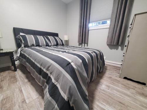 a bedroom with a bed with a striped comforter and a window at Modern Private 1BR Apt. w/Free Prkg + Fast Wi-Fi in Sault Ste. Marie