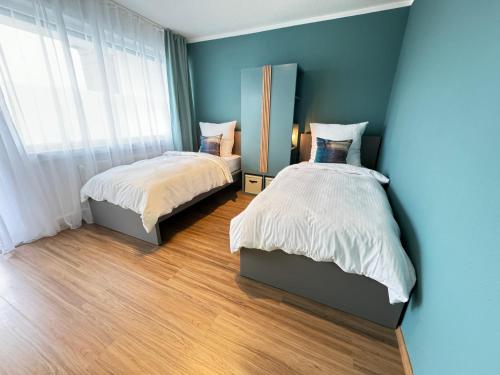 two beds in a bedroom with blue walls and wood floors at JUNX Bude in Marl