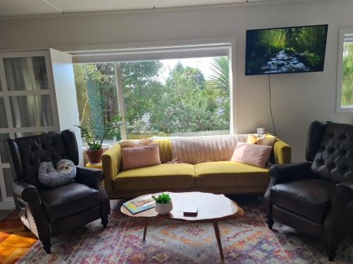 a living room with a yellow couch and two chairs at Paris studio in Auckland