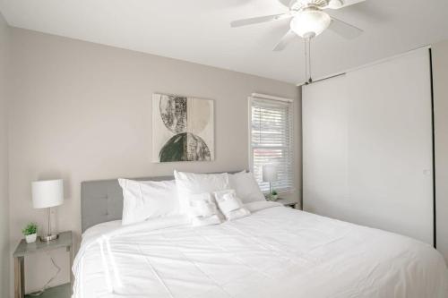 a white bedroom with a white bed with a ceiling fan at Enchanting Forestwood Retreat in Mobile