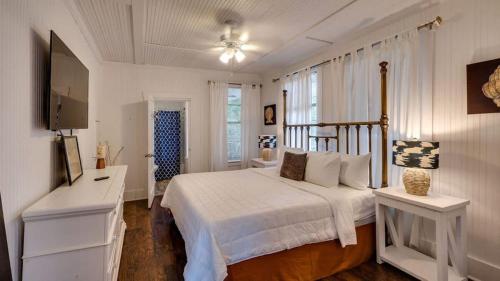 a white bedroom with a bed and a desk and a television at Flamingle in Fushia- Unit A- Steps to the Beach! in Tybee Island