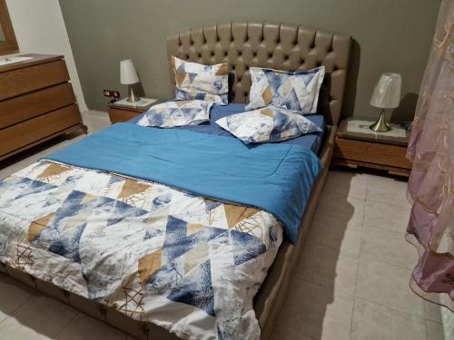 ein Schlafzimmer mit einem Bett mit einer blauen Bettdecke und Kissen in der Unterkunft Panorama III Cliniques les Jasmins in Ariana