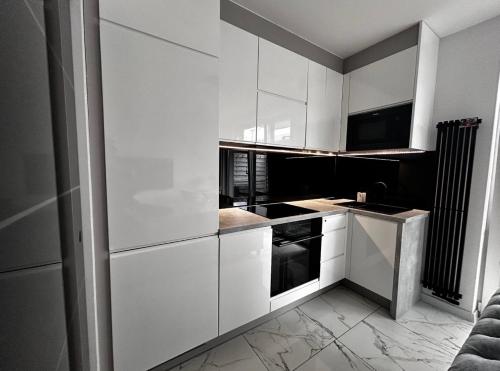 a white kitchen with white cabinets and black appliances at Apartament z tarasem in Gdańsk