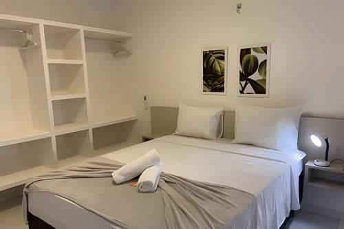 Hosts BR - Apartamentos funcionais في فورتاليزا: غرفة نوم بسرير ومخدات بيضاء ورفوف