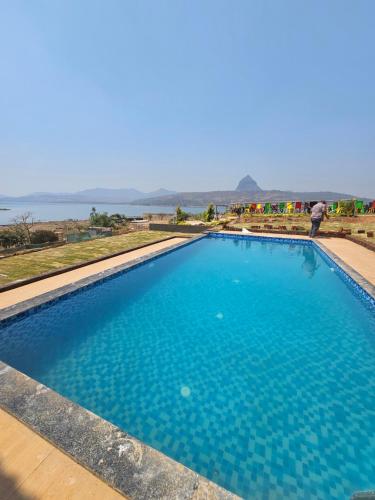 a large blue swimming pool with the ocean in the background at Plumeria Retreat pawna lakeside cottages in Malavli