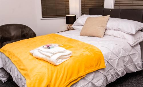 a bed with a yellow blanket and towels on it at Divine stay Nuneaton in Stockingford