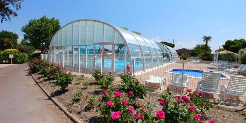 una casa de cristal con sillas y flores junto a una piscina en Holiday home on the island of Oleron in a residential park with heated swimming en Saint-Pierre-dʼOléron