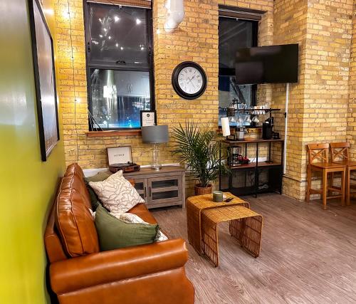 a living room with a couch and a clock on a brick wall at Heart of the City: Cozy 2-Bed Loft in Winnipeg