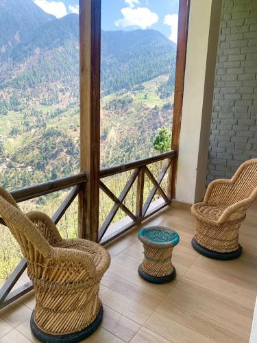 two chairs and a table on a balcony with a view at Apple Blush Retreat - Tirthan Valley in Gushaini