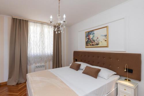 1 dormitorio con 1 cama blanca grande con lámpara de araña en Apartments Cime, en Dubrovnik