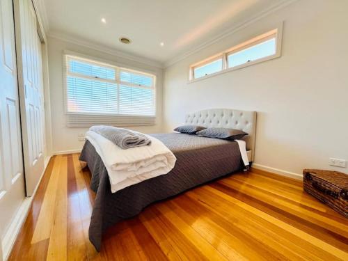 una camera da letto con un letto, pavimenti in legno e due finestre di Townhouse Near The World’s Coolest High st in 2024 a Melbourne