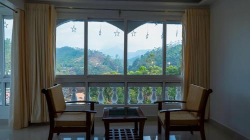 a room with a large window with two chairs and a table at Carmel Top Munnar in Munnar