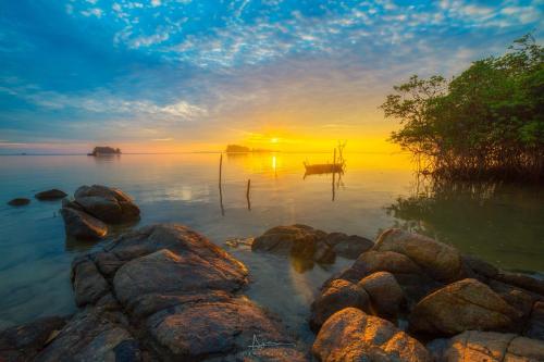 un coucher de soleil sur une étendue d'eau avec des rochers dans l'établissement LooLa Adventure Resort, à Telukbakau