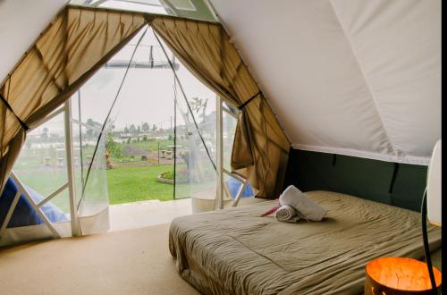 a bedroom with a bed in a tent with a large window at Popitan Garden Campground & Glamping Bedugul in Bedugul