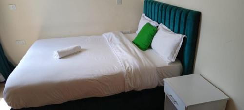 a white bed with green pillows and a box at SuperhostHomes AirBnbs Nakuru in Nakuru