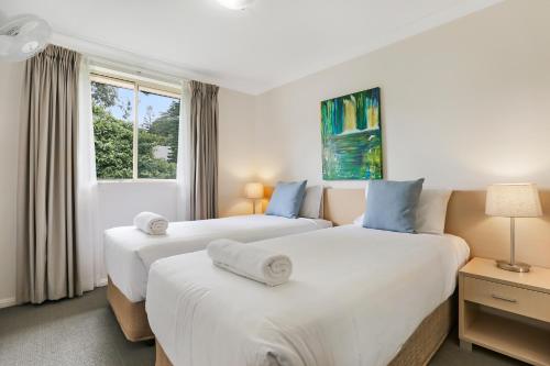 two beds in a white room with a window at Terralong Terrace Apartments in Kiama