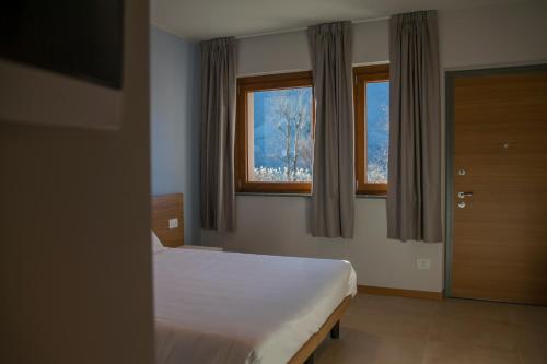 1 Schlafzimmer mit einem weißen Bett und 2 Fenstern in der Unterkunft Albergo La Romanella in Spinone Al Lago