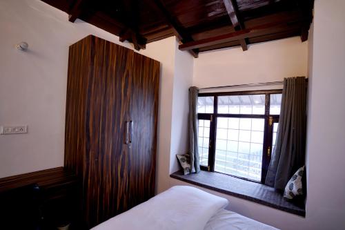 une chambre avec un lit et une grande fenêtre dans l'établissement HIMALAYANBLUES COTTAGES&STAYS, à Mukteswar