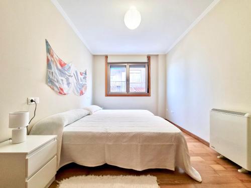 a white bedroom with a bed and a window at Apartamento en la playa! in Sanxenxo