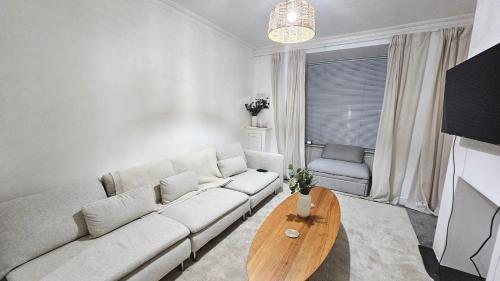 Hayes Deluxe Inn- London, Heathrow Airport في هايس: غرفة معيشة مع أريكة بيضاء وطاولة