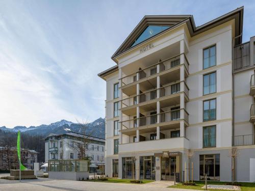 a large white building with mountains in the background at ibis Styles Bad Reichenhall in Bad Reichenhall