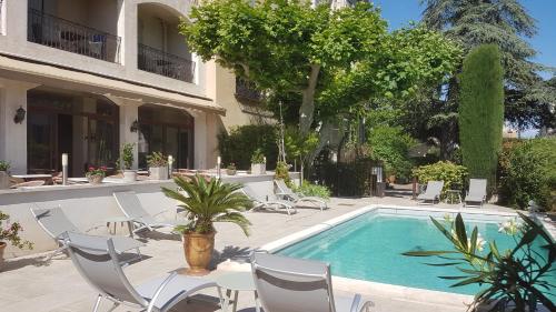 a swimming pool with chairs and a table and a building at Le Castelet des Alpilles in Saint-Rémy-de-Provence