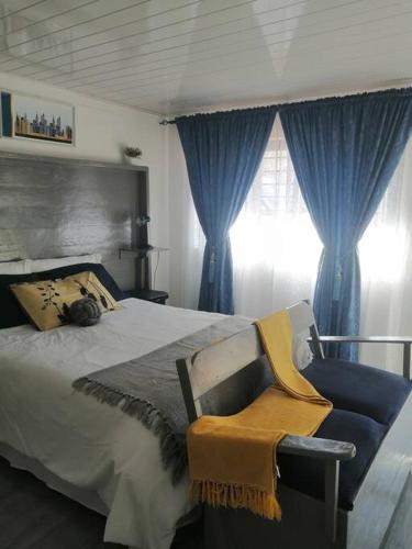 a bedroom with a bed with blue curtains and a chair at Ticia Apartment in Chipata