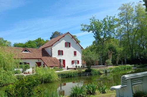 a white house with red windows next to a river at Le Moulin de Saubrigues in Saubrigues