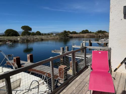 un banco rosa sentado en un muelle junto a un río en Marina / maison de pêcheur, en Le Barcarès