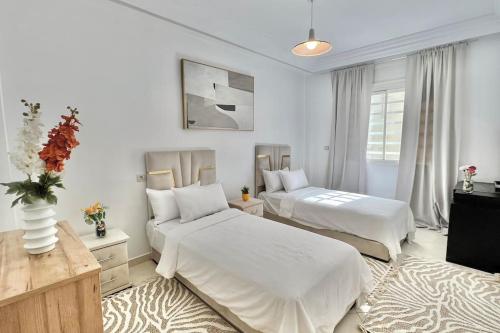 a white bedroom with two beds and a table at H9 Appartement flambant neuf au centre de Rabat Hassan in Rabat
