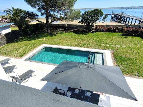 un parasol et des chaises à côté d'une piscine dans l'établissement Villa 12 pers avec piscine chauffée et vue exceptionnelle, première ligne Bassin d'Arcachon - FR-1-736-32, à Lège-Cap-Ferret